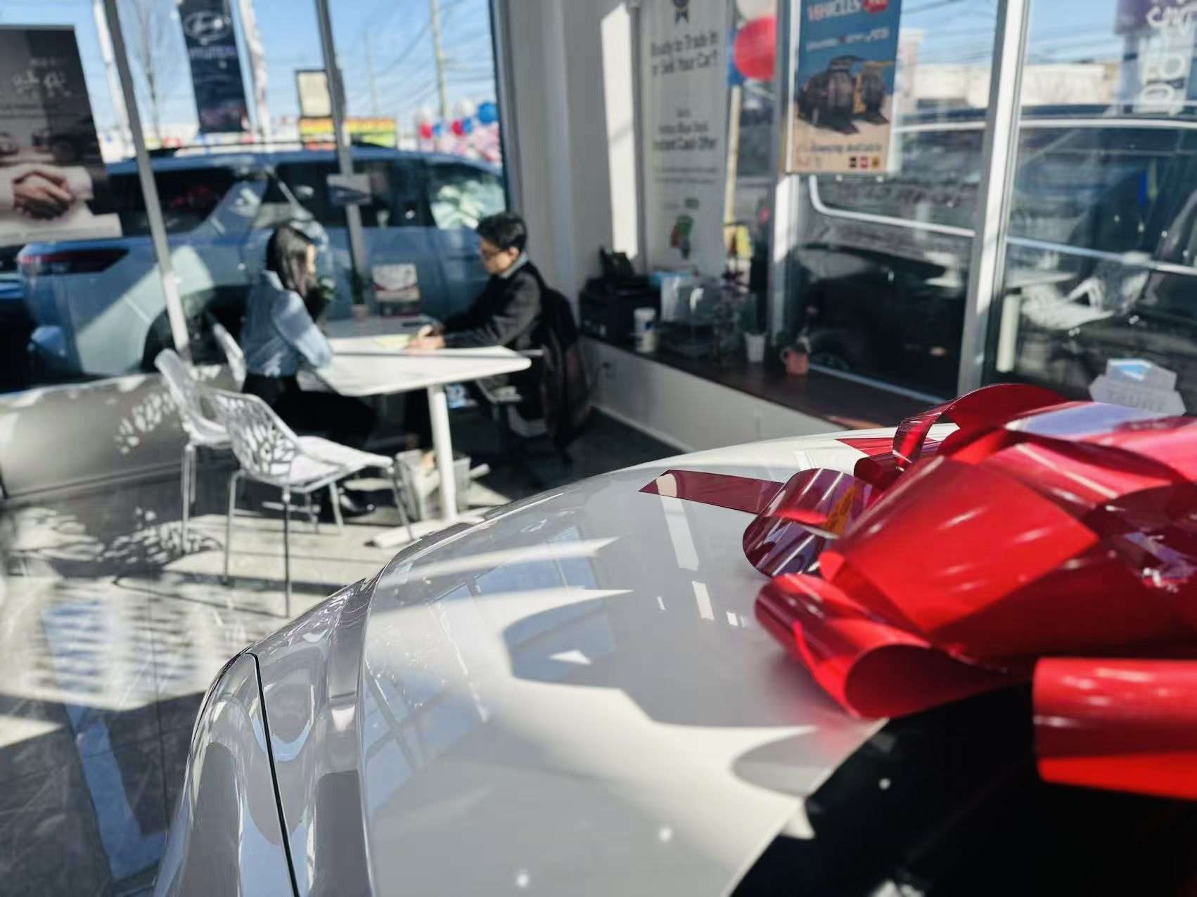 Inside a Staten Island car dealership, a red-bowed car and a sales meeting at Ideal Auto Sales Staten Island.